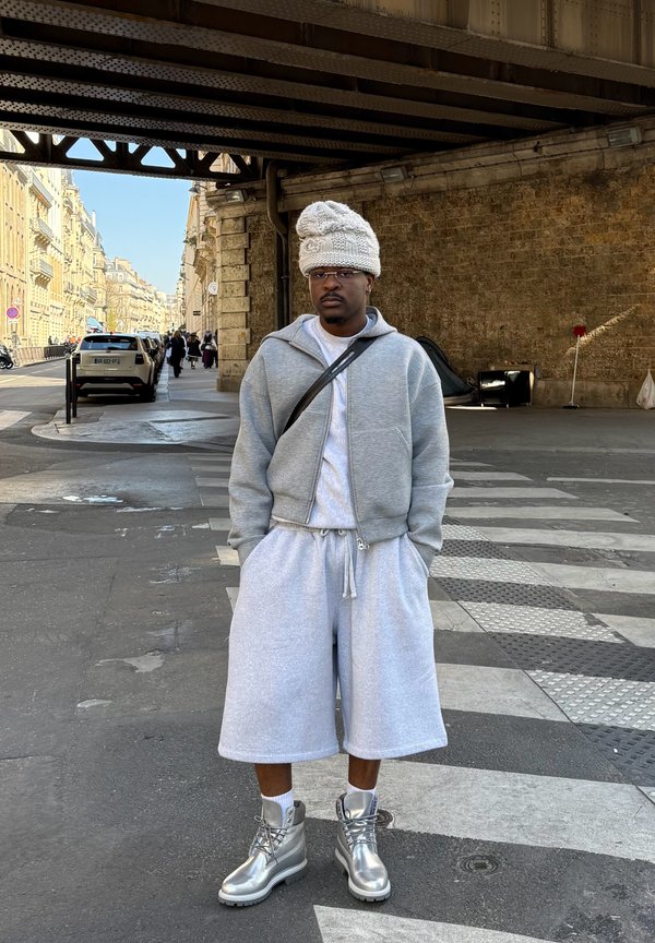 Sudadera gris con cremallera combinada con pantalones cortos a juego. Botas metálicas plateadas con calcetines blancos. Un gorro de punto texturizado en color crema completa el look.