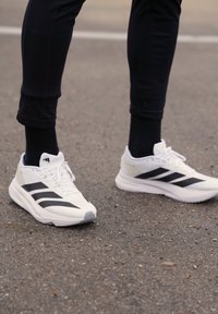 Chaussures de sport blanches avec des rayures noires et des accents gris. Conçues en mesh et en caoutchouc. Dotées d'un système de laçage et d'une semelle rembourrée.