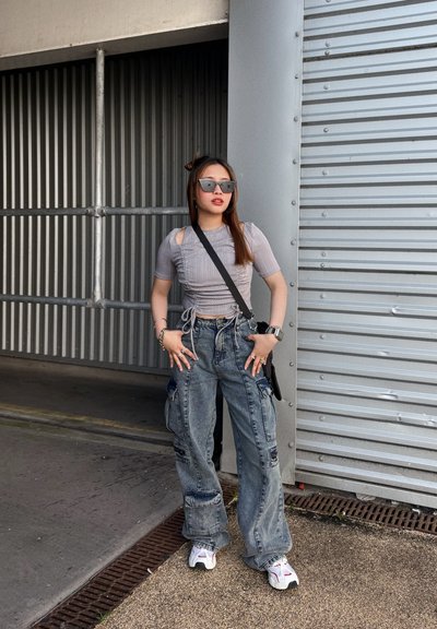 Top corto gris de canalé con recortes, pantalones cargo de gran tamaño y zapatillas blancas con acentos rojos. Los accesorios incluyen gafas de sol y pulseras.