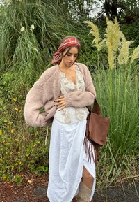 Cardigan de punto grueso color rosa claro sobre una blusa de ivoire con volantes, combinado con una falda blanca y un bolso de cuero marrón con flecos. Bufanda roja con estampado y botas beige.
