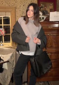 Veste extérieure grise sur un pull gris clair, pantalon noir et sac à main noir. Surfaces texturées et couches distinctes dans les vêtements.