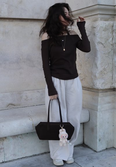 Top negro fuera de los hombros, pantalones blancos de pierna ancha y un bolso negro con un llavero de conejo de peluche. Diseño minimalista y texturas suaves.