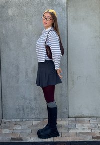 Cămașă cu mâneci lungi cu dungi, fustă plisată gri închis, dresuri bordo, cizme negre până la genunchi cu talpă platformă și o geantă de umăr burgundy.