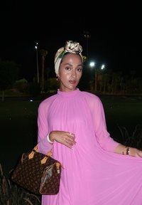 Rosa, flytende kjole med folder; en beige og brun Louis Vuitton-veske med detaljer. Modellen bærer et mønstret hodeplagg og smykker.