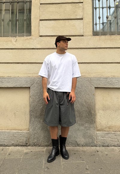 Camiseta blanca de gran tamaño, pantalones cortos grises y botas negras hasta el tobillo. Top de manga corta con un ajuste ligeramente holgado, pantalones cortos con un diseño relajado.