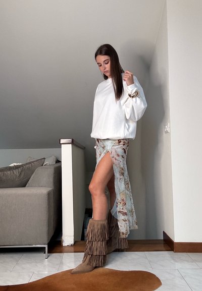 Sudadera blanca de gran tamaño, falda translúcida con flores y una abertura alta, y botas marrones con flecos. Texturas suaves y detalles de telas fluidas.