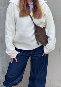 Fehér, texturált pulóver cipzáras gallérral, sötét farmer anyagú, széles szárú nadrággal párosítva. Barna szarvasbőr keresztpántos táska cipzárral.