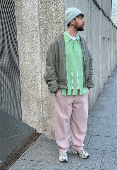 Suéter verde de punto con detalles recortados, chaqueta bomber gris, pantalones rosas y zapatillas grises, rematado con un gorro gris claro.