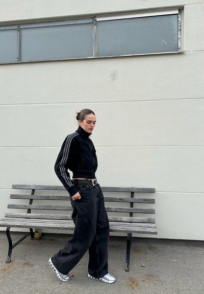 Chaqueta de pana negra ajustada con un cuello alto, mangas a rayas grises; combinada con pantalones de pierna ancha negros y zapatos metálicos plateados.