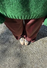 Grønn teksturert genser, burgunder bredbeinbukser og beige sneakers med mørke detaljer. Tatt ovenfra på en grusoverflate.
