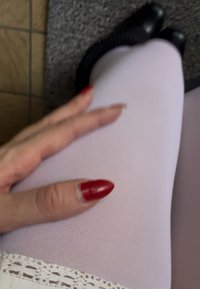 Ciorapi lavandă cu o textură netedă, complementați de o dantelă la bază. O mână cu unghii roșii se odihnește pe picior. Pantofi negri sunt vizibili.