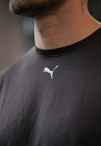 Czarny bawełniany t-shirt z okrągłym dekoltem i białym logo Puma na piersi. Gładka faktura z lekkimi zmarszczkami na materiale.