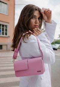 Ροζ δερμάτινη τσάντα με ορθογώνιο σχήμα, λεία επιφάνεια, κλείσιμο με καπάκι και αποσπώμενη θηλιά. Διαθέτει χρυσές μεταλλικές λεπτομέρειες.