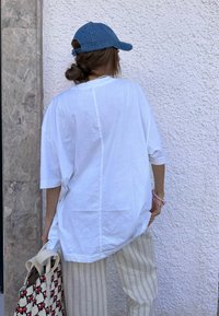 Hvid oversized skjorte med drop-skulder, parret med stribede bukser. En denimkasket og en mønstret totebag fuldender outfittet.