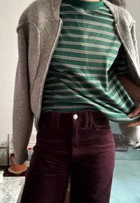 Grå lynlås cardigan over en grøn og stribet t-shirt, parret med høj talje bordeaux kordfløjl bukser med en metalsknap.