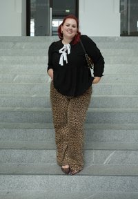 Μαύρη μπλούζα με λευκή λεπτομέρεια σε φιόγκο, συνδυασμένη με παντελόνι φαρδύ με λεοπάρ σχέδιο και μυτερές γόβες. Τοποθετημένη σε γκρι πέτρινες σκάλες.