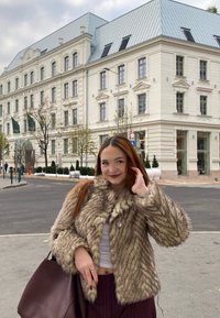 Ψεύτικο φουσκωτό μπουφάν σε μπεζ και καφέ αποχρώσεις με ραβδωτή υφή, που διαθέτει λεπτομέρεια κουμπιού. Σκούρα τσάντα χ�ειρός και ριγέ παντελόνι συνδυασμένο με λευκή μπλούζα.