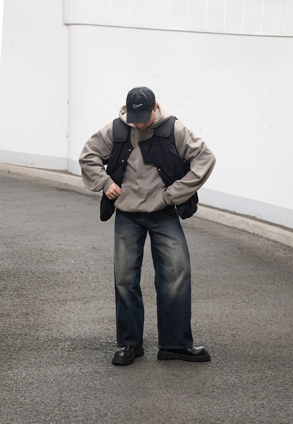 Casualny strój z czarną bezrękawniką, szarym hoodie, szerokimi, wyblakłymi niebieskimi dżinsami oraz masywnym, czarnym obuwiem. Czapka w kolorze czarnym dopełnia całość.