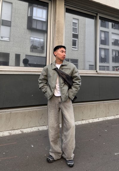 Chaqueta verde claro, de gran tamaño, con un bolsillo con cremallera, camisa blanca debajo, jeans grises holgados y zapatos negros con un patrón sutil.