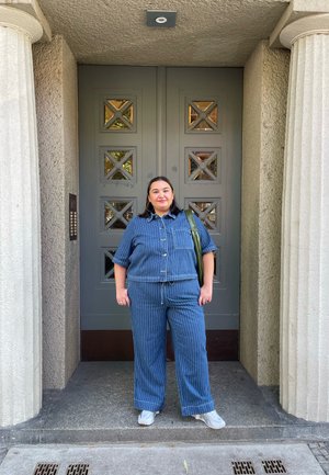 Conjunto de denim que incluye una camisa de manga corta con botones y pantalones de pierna ancha con rayas verticales. Al fondo, se observa una puerta gris texturizada.