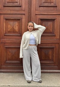 Kremowy kardigan, jasno-niebieski top cropped i szare, paskowane spodnie typu wide-leg. Materiał wydaje się miękki; kardigan ma guziki i luźne rękawy.