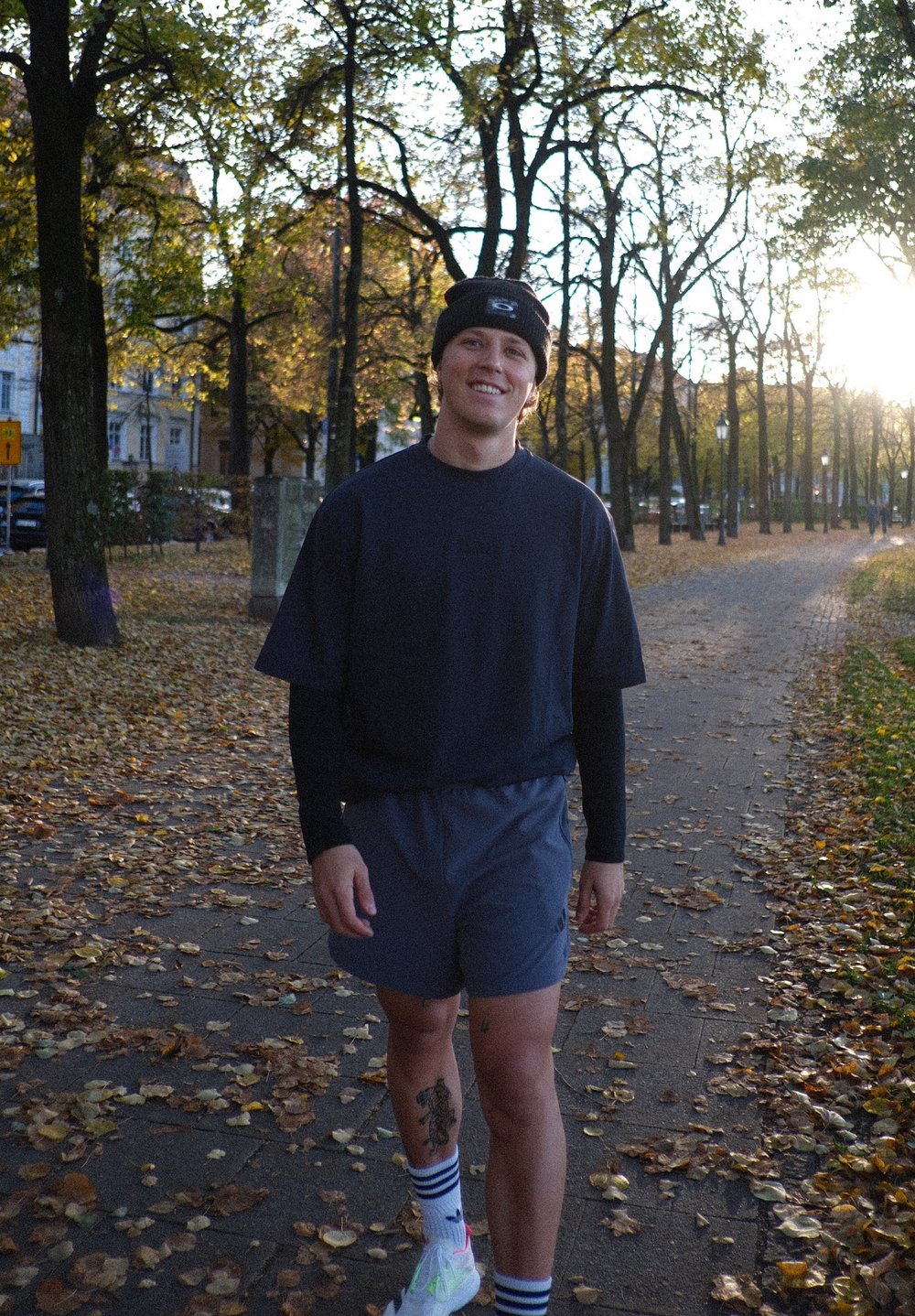 Sportowy strój składający się z ciemnej koszulki z krótkim rękawem i szarych szortów. Akcesoria to czarna czapka beanie oraz białe sneakersy z kolorowymi akcentami.