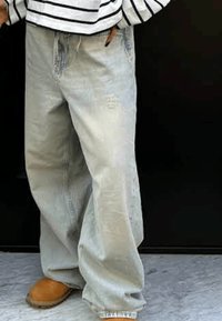 Helleblaue, weit geschnittene Jeans aus Denim mit einem abgedunkelten Finish und distressed Details, kombiniert mit beigen Slippern.