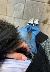 Cinturón negro con herrajes plateados, jeans azul claros, camiseta blanca y zapatillas negras con acentos blancos y amarillos sobre una superficie de piedra.