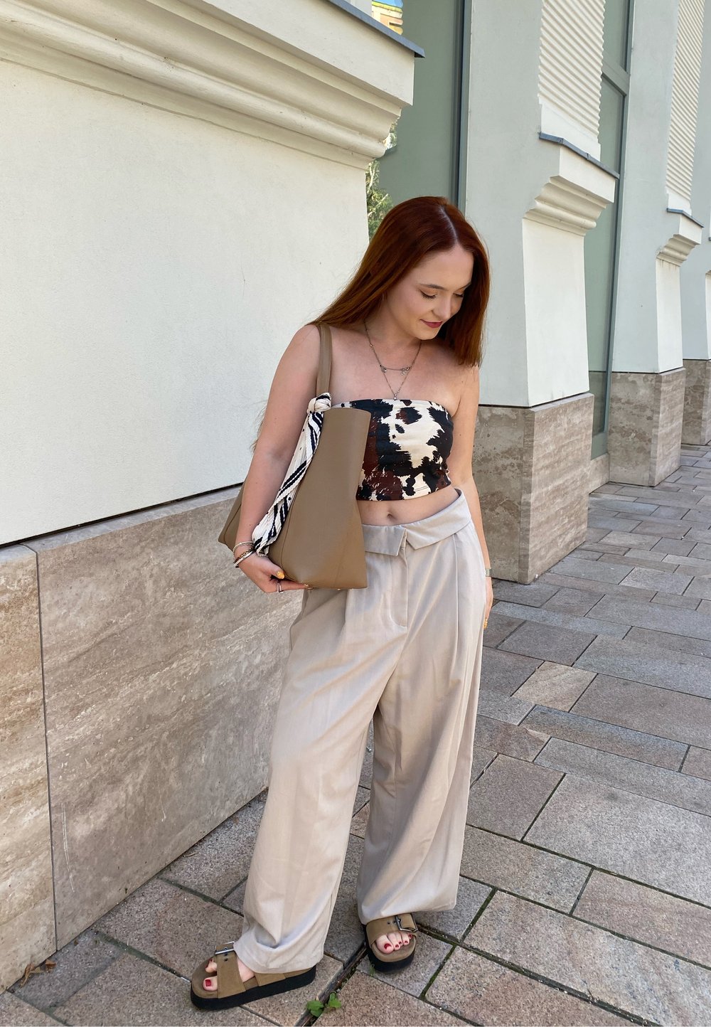 Top senza spalline a fantasia bianco e nero, pantaloni beige chiaro a gamba larga, borsa marrone e sandali scuri. Tessuti morbidi e vestibilità rilassata.