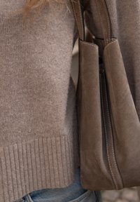 Suéter castanho tricotado, com bainha canelada, combinado com uma mala de camurça castanha suave, apresentando uma textura lisa e costura branca em contraste.