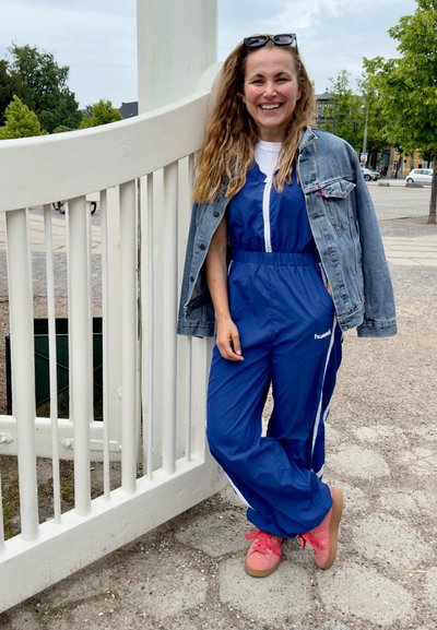 Un mono azul con detalles blancos, un cierre frontal y una cinturilla elástica, combinado con una chaqueta de mezclilla y zapatillas rosas.