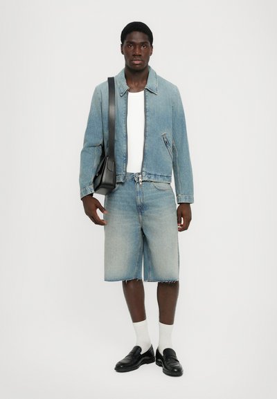 Chaqueta de denim azul claro con cremallera frontal, combinada con pantalones cortos de denim a juego. Un bolso de cuero negro y mocasines complementan el conjunto.