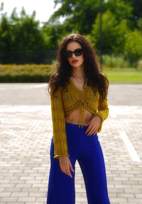 Žlutý pletený zkrácený svetr s tkaničkou, ve spojení s modrými kalhotami s širokými nohavicemi. Modelka má na sobě černé sluneční brýle a vrstvené náhrdelníky.