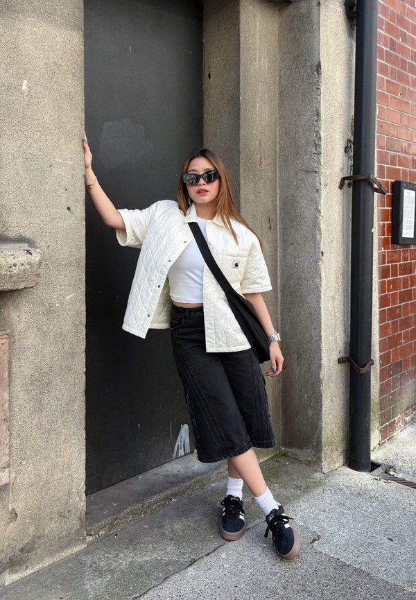 Quilted white short jacket over a white crop top, teamed with black cargo shorts and black sneakers featuring patterned soles. Black sunglasses.