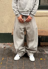 Harmaa vetoketjullinen huppari, jossa etutasku, yhdistettynä väljälahkeisiin harmaisiin collegehousuihin, joissa on kiristysnauha vyötäröllä ja sivutaskut. Valkoiset lenkkarit.