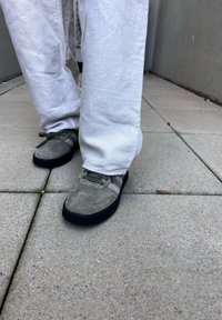 Gray suede shoes with black rubber soles, featuring light gray accents. Loose-fitting white pants are worn over the shoes.