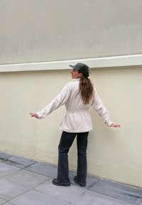 Veste en polaire beige avec une taille à cordon de serrage, manches longues et coupe décontractée, associée à un jean noir évasé et des bottes noires.