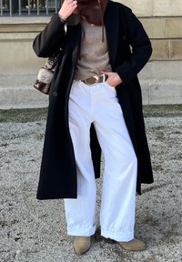 Mustad kahekordne jope, beež kampsun, valged laiad püksid, pruun vöö, helepruun ankle saapad. Hoidab väikest pruuni kotti. Välitingimused.