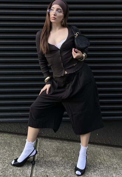 Cárdigan negro de canalé, culottes anchos negros, calcetines blancos con volantes y sandalias de tacón negras. Los accesorios incluyen un bolso redondo negro y pulseras de oro.