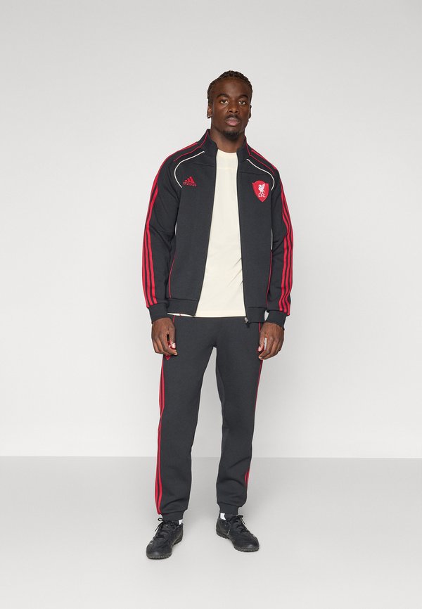 Completo sportivo nero con strisce rosse, dotato di un logo sulla giacca. L'insieme presenta una chiusura frontale con zip ed è abbinato a sneakers nere.