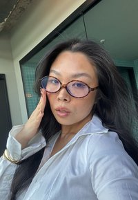 Silkkireunaiset tortoiseshell-lasit sinisävyisillä linsseillä, yhdistettynä valkoiseen nappipaitaan, hopeiseen korukäsikoruukkoihin ja pitkään mustaan hiukseen.