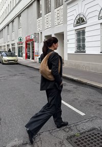 Črne prugaste hlače, črn blazer in torba iz zamsha v svetlo rjavi barvi. Oseba hodi po ulici, v ozadju pa je trgovina Spar.