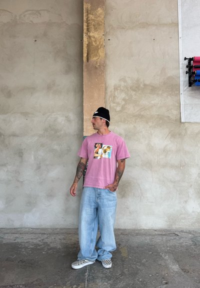 Camiseta de algodón rosa con un gráfico central, combinada con jeans de mezclilla azul claro holgados y zapatillas de lona a cuadros. Gorro negro.