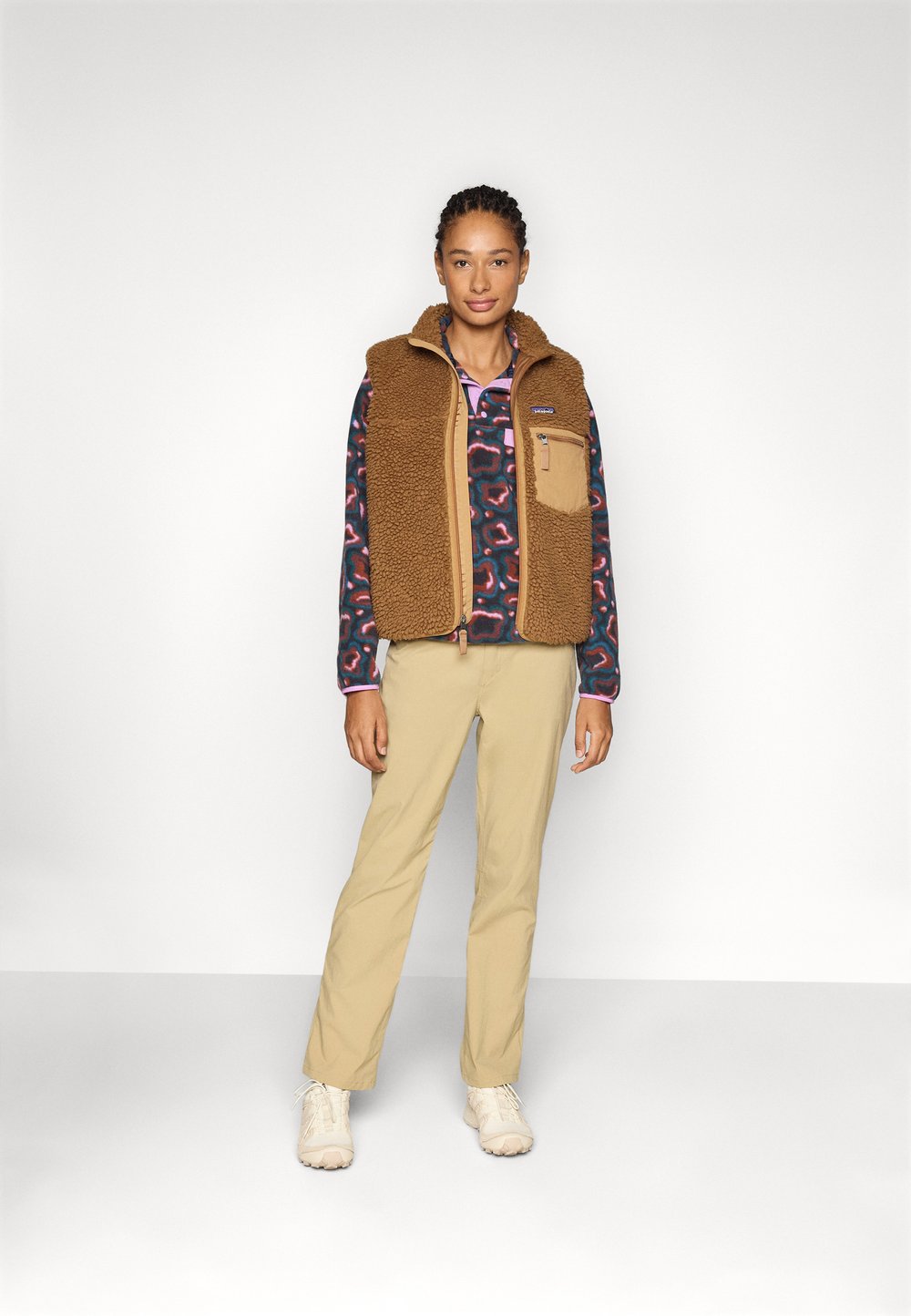 Rjav flisast telovnik preko vzorčaste srajce, bež hlače in svetlo obutev. Ima žepke in visok ovratnik. Preprost dizajn.