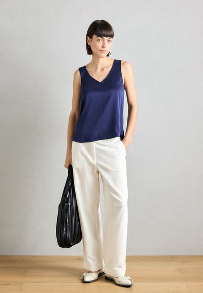 Top sin mangas de satén azul marino con escote en V, combinado con pantalones anchos de canalé blancos. Los accesorios incluyen un bolso negro de gran tamaño y zapatos blancos.