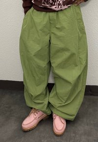 Pantalon vert, ample et taille haute avec une texture lisse. Porté avec des chaussures bateau roses dotées d'une semelle texturée et de lacets.