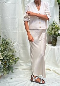 Lys beige cropped cardigan med rullede �ærmer og tre knapper, parret med en lang, glat satin cremeskirt og sølv sandaler.