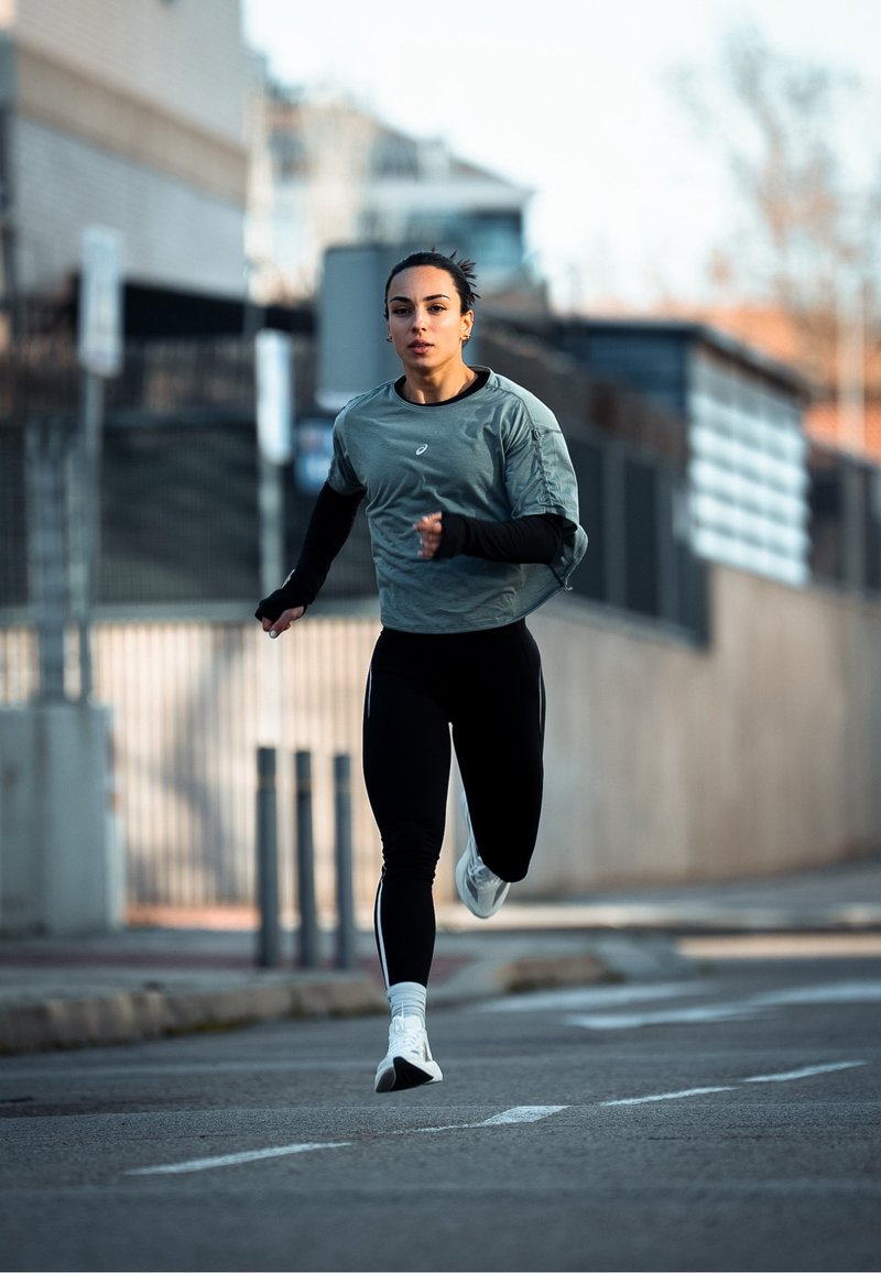 Nő sportos ruhában fut egy városi utcán, háttérben épületekkel és akadályokkal, nappali fényben.