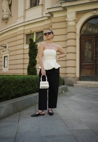 Top peplum blanco, pantalones de pierna ancha negros, bailarinas negras y un mini bolso blanco. Las gafas de sol y los accesorios dorados completan el look.