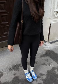 Črni puhasti pulover, črne legice, rjava usnjena torba, modri supergi z belimi črtami in kremno-bele pletene nogavice.